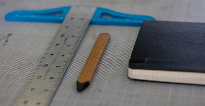 a T-square, Walnut Pencil, and moleskine journal on a grid mat