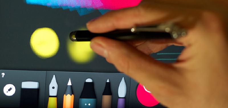 Hand holding a with capacitive stylus to blur a yellow circle on a gray background in Paper for iPadOS.