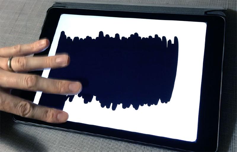 Fingers moving across an iPad’s screen to fill in a black background in Paper app/