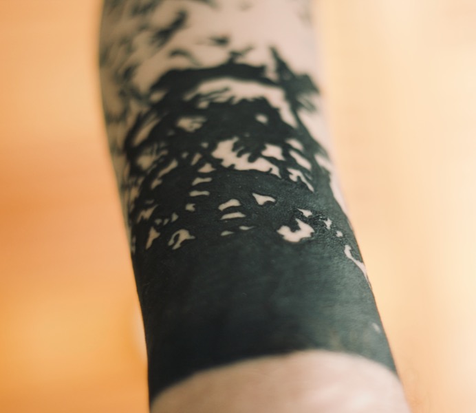 Black arm tattoo of trees and birds.